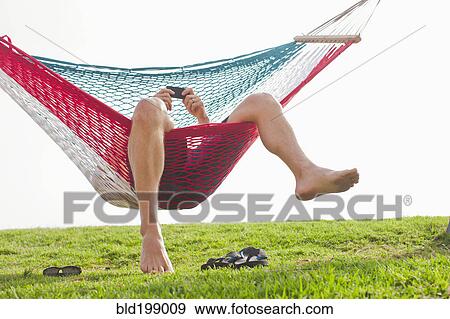 Stock Photo - Caucasian man relaxing in hammock with cell phone. Fotosearch