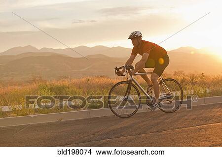 Picture - Caucasian man riding bicycle on remote road. Fotosearch