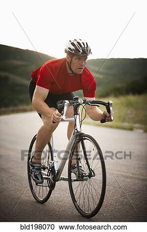 Stock Image - Caucasian man riding bicycle on remote road. Fotosearch