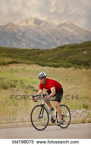 Stock Image - Caucasian man riding bicycle on remote road. Fotosearch