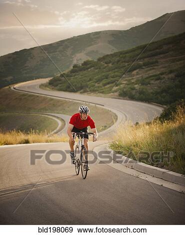 Stock Photo - Caucasian man riding bicycle on remote road. Fotosearch
