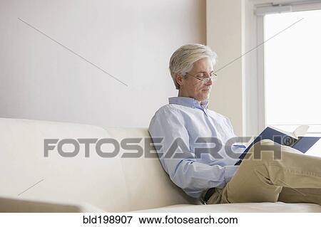 Stock Photo - Caucasian man sitting on sofa reading book. Fotosearch