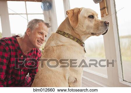 Stock Image - Caucasian man sitting with labrador. Fotosearch