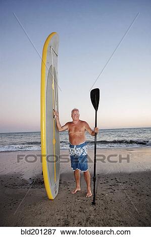 Stock Photo - Caucasian man standing with paddleboard. Fotosearch