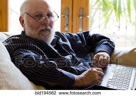 Stock Image - Caucasian man using laptop on sofa. Fotosearch