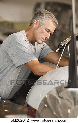 Stock Image - Caucasian man working in airplane hangar. Fotosearch