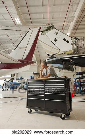 Stock Photo - Caucasian man working in airplane hangar. Fotosearch