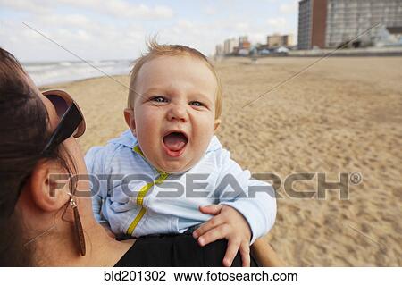 Stock Image - Caucasian mother holding baby boy on beach. Fotosearch