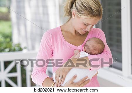 Stock Image - Caucasian mother holding baby on porch. Fotosearch