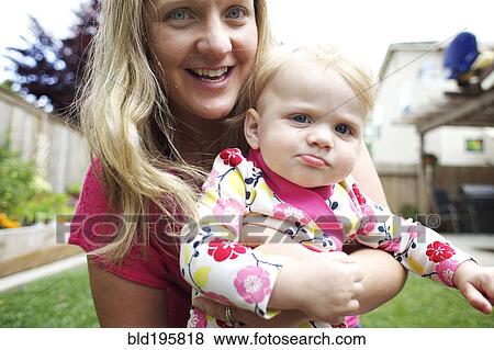 Stock Photo - Caucasian mother holding daughter in backyard. Fotosearch
