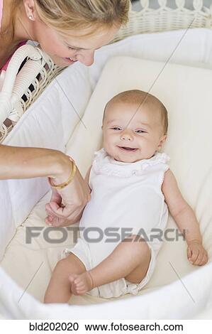 Stock Image - Caucasian mother looking at baby in bassinet. Fotosearch