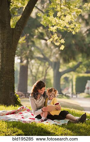 Stock Photography - Caucasian mother reading story to daughter in park. Fotosearch
