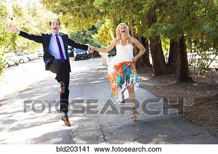 Stock Image - Caucasian newlywed couple skipping on road. Fotosearch