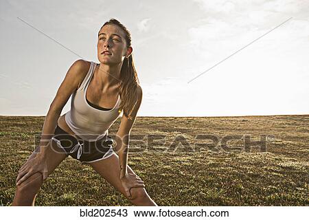 Stock Image - Caucasian runner stretching in field. Fotosearch