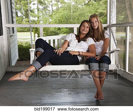 Stock Photo - Caucasian sisters sitting on porch swing together. Fotosearch