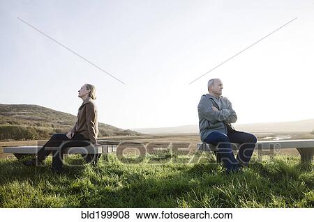 Stock Photo - Caucasian sitting back to back on benches at beach. Fotosearch