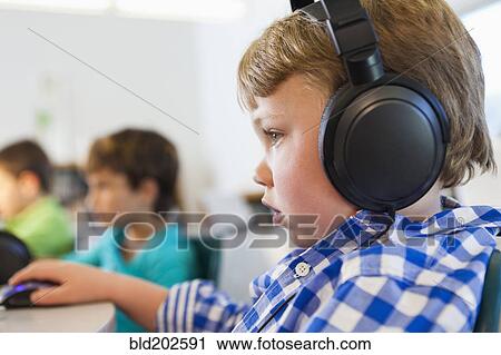 Stock Image - Caucasian student listening to headphones in classroom. Fotosearch