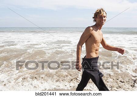 Stock Image - Caucasian surfer walking on beach. Fotosearch