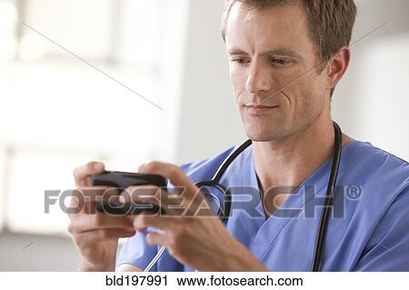 Stock Image - Caucasian surgeon text messaging on cell phone. Fotosearch
