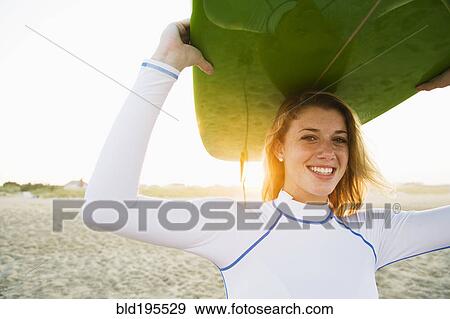 Stock Photo - Caucasian teenage girl holding surfboard overhead on beach. Fotosearch