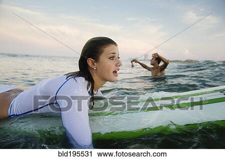 Stock Image - Caucasian teenage girl paddling on surfboard in ocean. Fotosearch