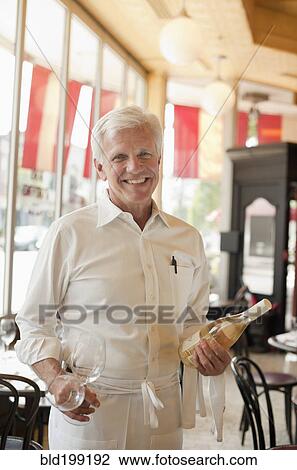 Stock Image - Caucasian waiter holding bottle of white wine. Fotosearch