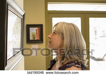 Stock Photograph - Caucasian woman admiring painting in gallery. Fotosearch
