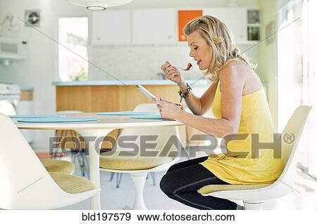 Caucasian woman eating and using digital tablet in dining room View Large Photo Image Stock Photo - Caucasian woman eating and using digital tablet in dining room. Fotosearch