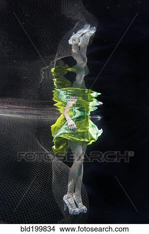 Picture - Caucasian woman in dress swimming under water. Fotosearch