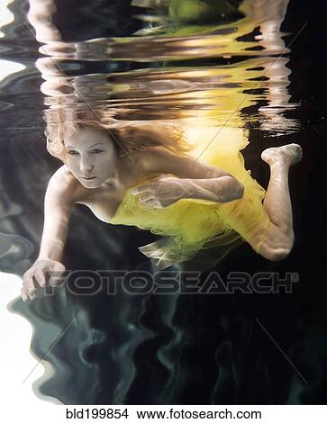 Picture - Caucasian woman in dress swimming under water. Fotosearch