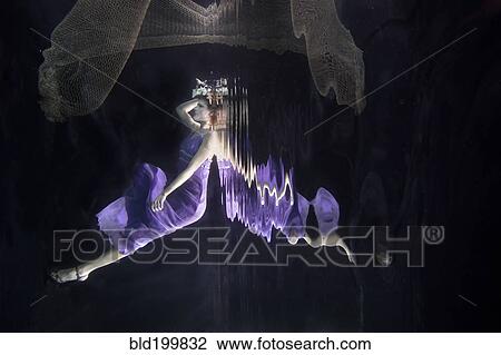 Stock Image - Caucasian woman in dress swimming under water. Fotosearch