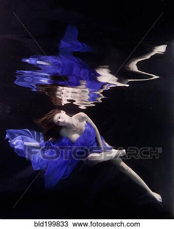 Stock Image - Caucasian woman in dress swimming under water. Fotosearch