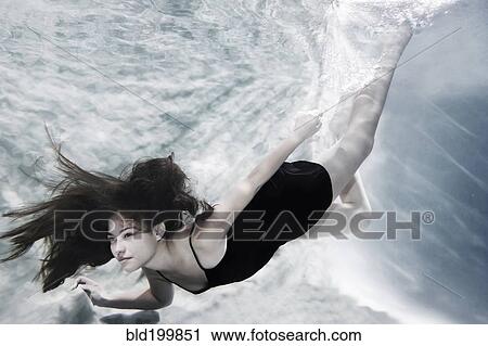 Stock Image - Caucasian woman in dress swimming under water. Fotosearch