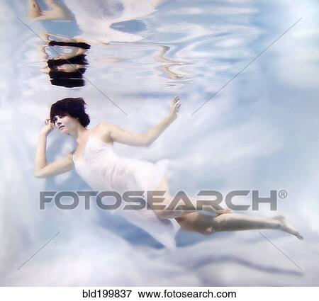 Stock Photo - Caucasian woman in dress swimming under water. Fotosearch