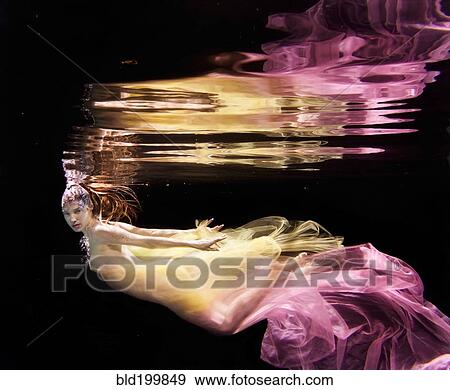 Stock Photo - Caucasian woman in dress swimming under water. Fotosearch