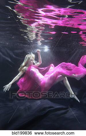 Stock Photograph - Caucasian woman in dress swimming under water. Fotosearch