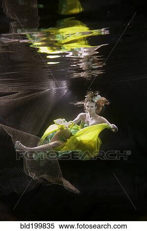 Stock Photography - Caucasian woman in dress swimming under water. Fotosearch