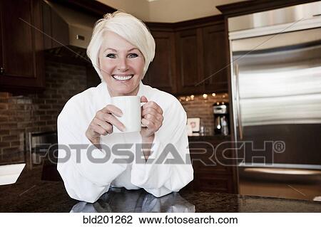 Stock Image - Caucasian woman in robe drinking coffee. Fotosearch