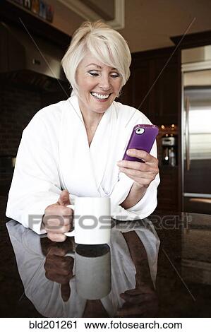 Stock Image - Caucasian woman in robe using cell phone. Fotosearch