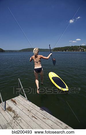 Caucasian woman jumping in lake next to paddleboard View Large Photo Image Stock Image - Caucasian woman jumping in lake next to paddleboard. Fotosearch