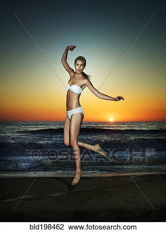 Stock Image - Caucasian woman jumping on beach. Fotosearch