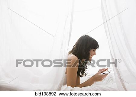 Stock Image - Caucasian woman laying in bed listening to mp3 player. Fotosearch