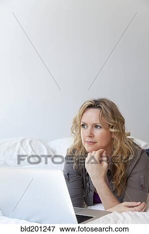 Caucasian woman laying on bed using laptop View Large Photo Image Stock Photo - Caucasian woman laying on bed using laptop. Fotosearch