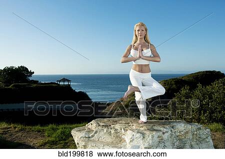 Stock Photo - Caucasian woman practicing yoga near ocean. Fotosearch