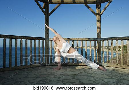 Stock Photograph - Caucasian woman practicing yoga near ocean. Fotosearch