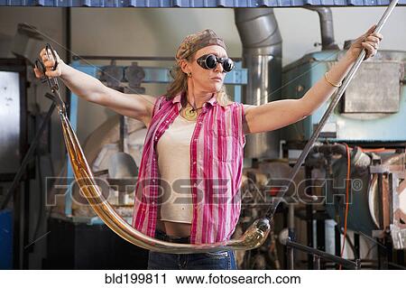 Stock Image - Caucasian woman pulling glass in glass blowing studio. Fotosearch