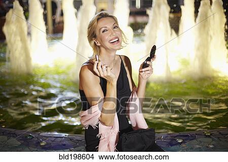 Picture - Caucasian woman putting on make up near fountain. Fotosearch