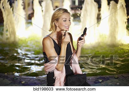 Stock Image - Caucasian woman putting on make up near fountain. Fotosearch