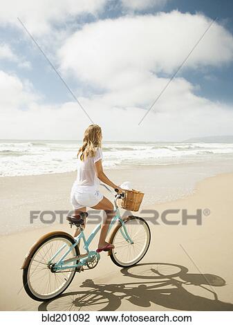 Stock Image - Caucasian woman riding bicycle on beach. Fotosearch