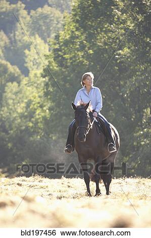 Stock Photograph - Caucasian woman riding horse in field. Fotosearch